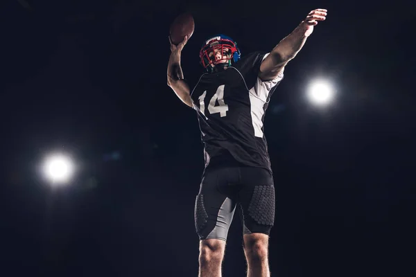Вид снизу американского футболиста бросающего мяч под прожекторами на черном — стоковое фото