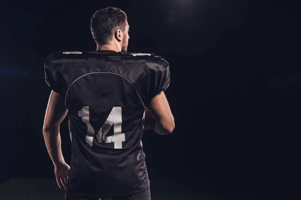 Vista posteriore del giocatore di football americano in uniforme nera isolato su nero — Foto stock