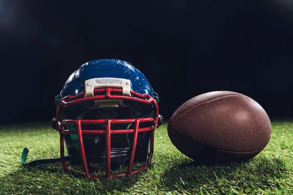 Close-up shot of american football helmet with ball on green grass on black — Stock Photo
