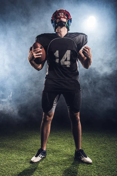 American football player with ball making fist and looking up against white smoke — Stock Photo