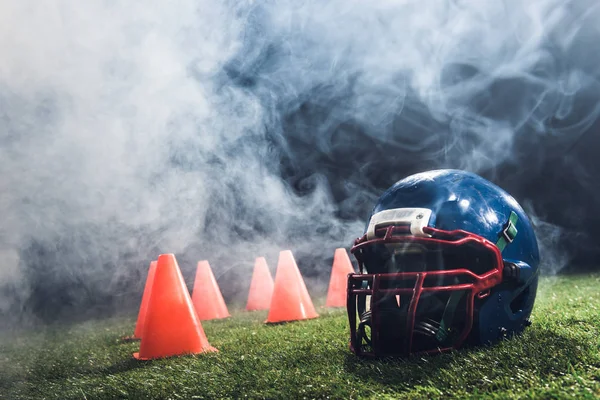 Primo piano colpo di casco da football americano con coni su erba verde con fumo bianco sopra — Foto stock