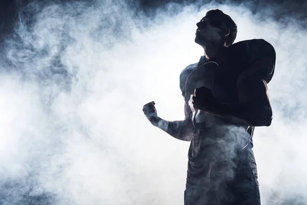 Bottom view of emotional american football player making fists and looking up against white smoke — Stock Photo