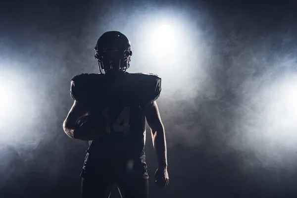 Silhouette scura del giocatore di football americano attrezzato con palla contro il fumo bianco — Foto stock