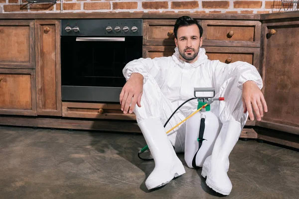 Tired pest control worker sitting on floor in kitchen and looking at camera — Stock Photo