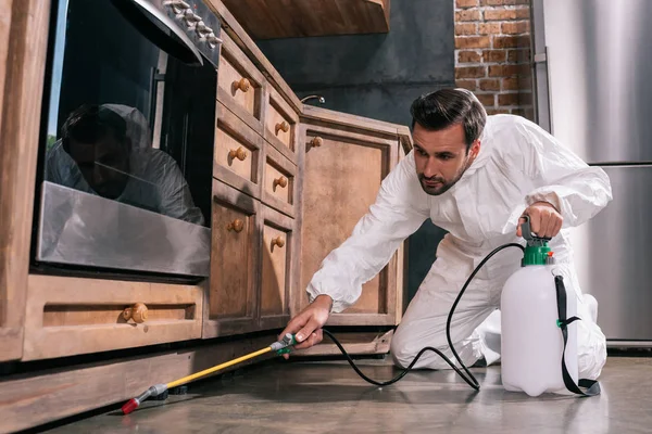 Side view of pest control worker spraying pesticides under cabinet in kitchen — Stock Photo