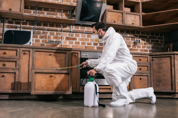 Pest control worker spraying pesticides in cabinet in kitchen — Stock Photo