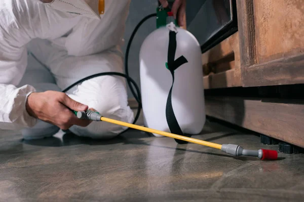 Imagen recortada del trabajador de control de plagas rociando pesticidas en el suelo en la cocina - foto de stock