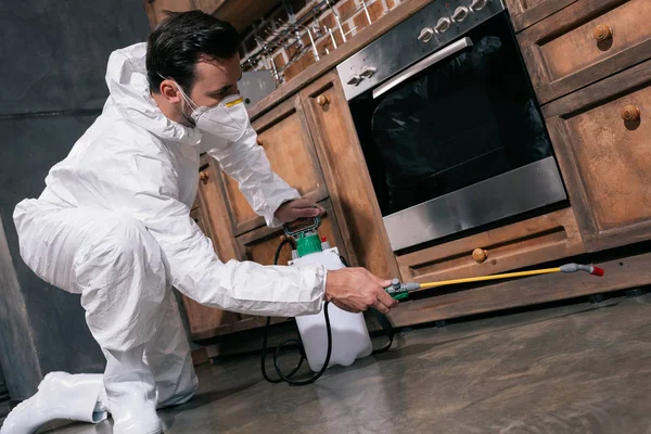 Trabajador de control de plagas pulverización de pesticidas debajo del gabinete en la cocina - foto de stock