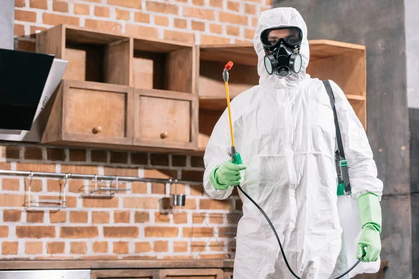 Pest control worker in uniform standing with sprayer in kitchen — Stock Photo