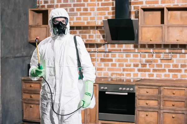 Trabajador de control de plagas de pie con pulverizador en la cocina - foto de stock