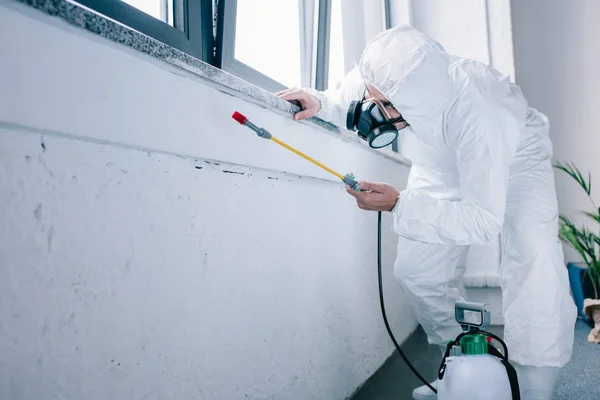 Trabajador de control de plagas pulverización de productos químicos bajo el alféizar de la ventana en casa - foto de stock