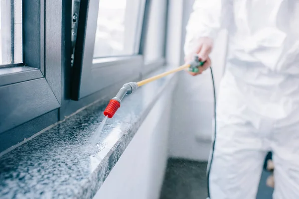 Imagen recortada del trabajador de control de plagas rociando pesticidas en el alféizar de la ventana en casa - foto de stock