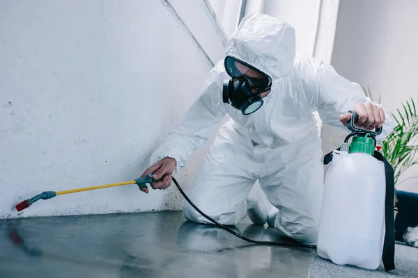 Trabajador de control de plagas pulverización de pesticidas en el suelo en casa - foto de stock