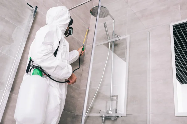 Low angle view of pest control worker spraying pesticides with sprayer in bathroom — Stock Photo