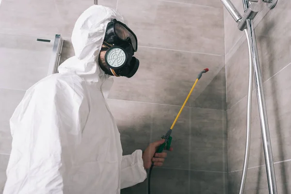 Pest control worker in respirator spraying pesticides with sprayer in bathroom — Stock Photo