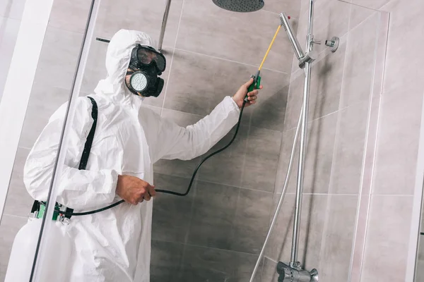 Trabajador de control de plagas pulverización de pesticidas con pulverizador en el baño - foto de stock