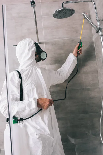 Vista lateral del trabajador de control de plagas pulverización de pesticidas con pulverizador en el baño - foto de stock