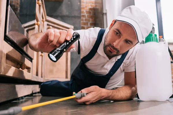 Trabajador de control de plagas acostado en el suelo y rociando pesticidas en la cocina - foto de stock