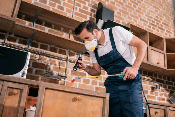 Pest control worker spraying pesticides in kitchen and using flashlight — Stock Photo