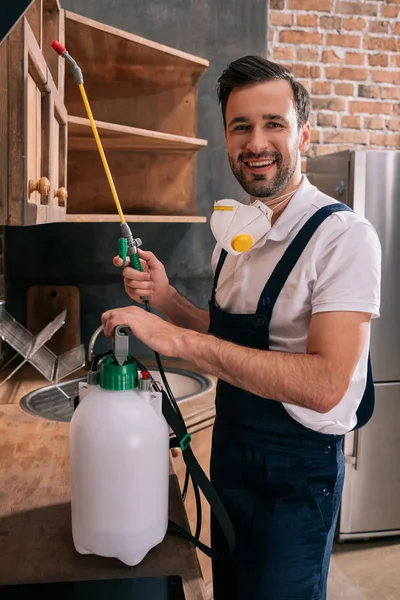 Sorrindo pragas trabalhador de controle segurando pulverizador na cozinha — Fotografia de Stock