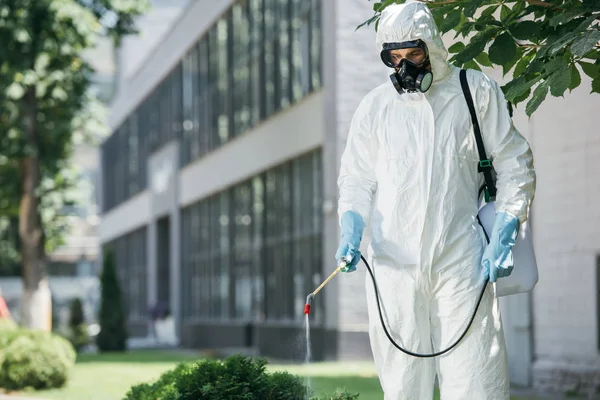 Pest control worker in uniform and respirator spraying pesticides on street with sprayer — Stock Photo