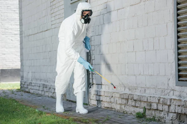 Trabajador de control de plagas pulverización de productos químicos con pulverizador en la pared del edificio - foto de stock