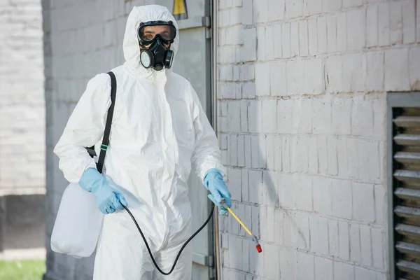 Schädlingsbekämpfer in Atemschutzmaske sprüht Pestizide mit Sprüher an Hauswand — Stockfoto