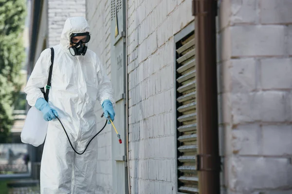 Trabalhador de controle de pragas pulverizando pesticidas com pulverizador na parede da construção na rua — Fotografia de Stock