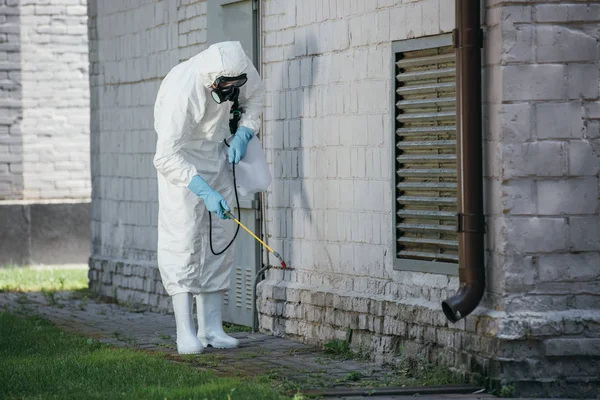 Trabajador de control de plagas pulverización de pesticidas con pulverizador en la pared del edificio - foto de stock