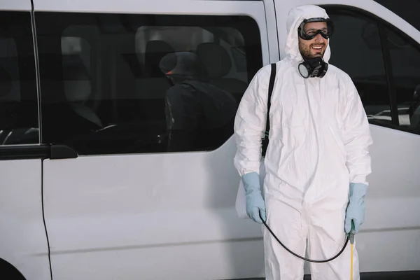 Pest control worker in uniform standing near car on street and holding sprayer — Stock Photo