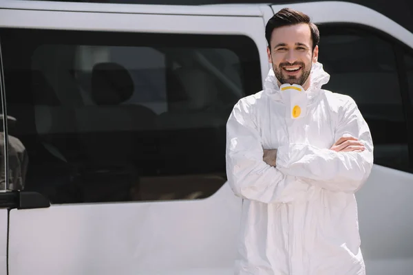 Felice disinfestatore in uniforme in piedi con le braccia incrociate vicino auto sulla strada — Foto stock