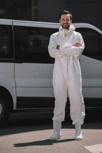 Smiling pest control worker with crossed arms looking at camera near car on street — Stock Photo