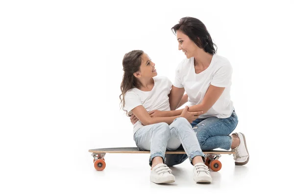 Mère assise près de fille souriante sur planche à roulettes isolée sur blanc — Photo de stock