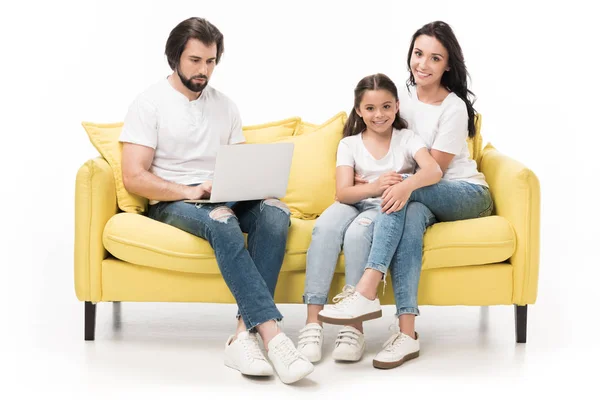 Зосереджений чоловік використовує ноутбук з сім'єю відпочиває на дивані поруч ізольовано на білому — стокове фото