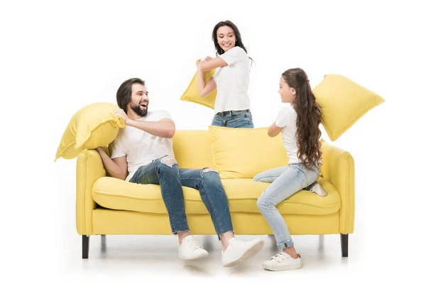 Família feliz em camisas brancas no sofá amarelo tendo travesseiro luta isolada no branco — Fotografia de Stock