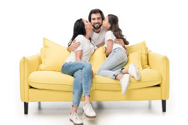 Mutter und Tochter auf gelbem Sofa küssen glücklichen Vater isoliert auf weißem Grund — Stockfoto