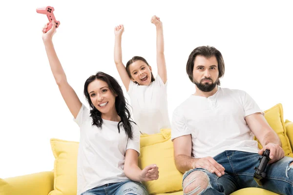 Feliz madre e hija en el sofá amarillo jugando videojuegos con el padre molesto cerca de aislado en blanco - foto de stock