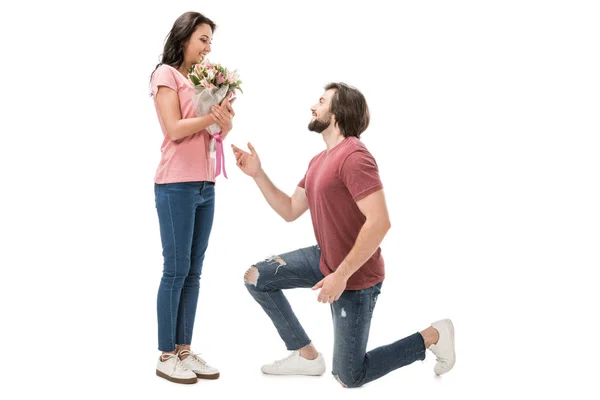 Vista lateral de la mujer con ramo de flores y el hombre de pie sobre una rodilla aislado en blanco - foto de stock