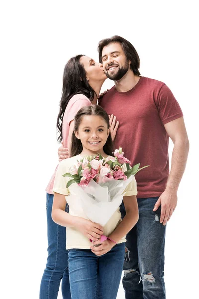 Porträt einer lächelnden Tochter mit einem Blumenstrauß und Eltern, die sich hinter isoliert auf weiß küssen — Stockfoto