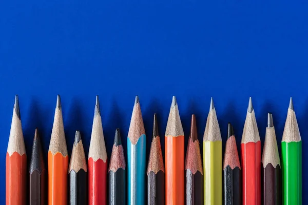 Vista superior de varios lápices coloridos colocados en fila sobre fondo azul - foto de stock