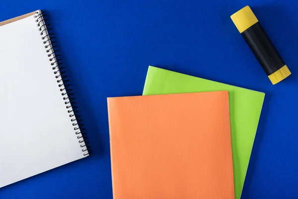 Vista superior de notebook em branco, vara de cola e livros didáticos sobre fundo azul — Fotografia de Stock