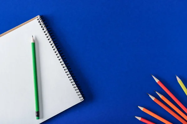 Top view of arranged variety pencils and blank textbook on blue background — Stock Photo