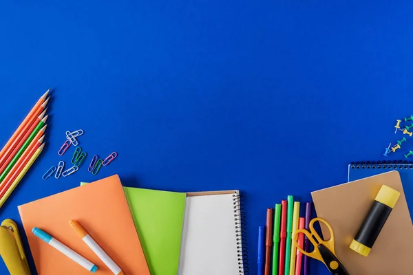 Draufsicht auf leeres Lehrbuch und vielfältige Schreibwaren auf blauem Hintergrund — Stockfoto