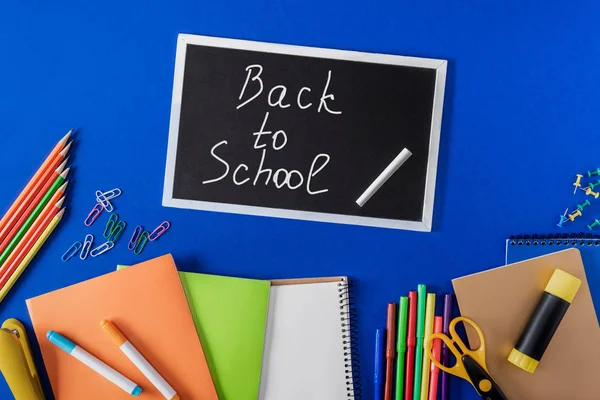 Top view of chalkboard with lettering back to school and variety stationery on blue background — Stock Photo