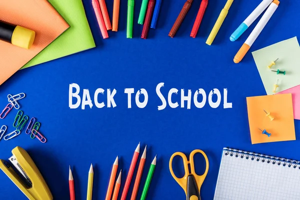 Vista dall'alto di lettering torna a scuola da carta bianca circondata da cancelleria varietà su sfondo blu — Foto stock