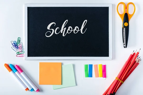 Top view of chalkboard with lettering school and arranged variety stationery on white background — Stock Photo