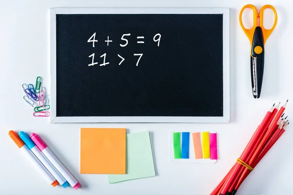 Vista dall'alto della lavagna con somme di matematica e varietà di materiale scolastico su sfondo bianco — Foto stock