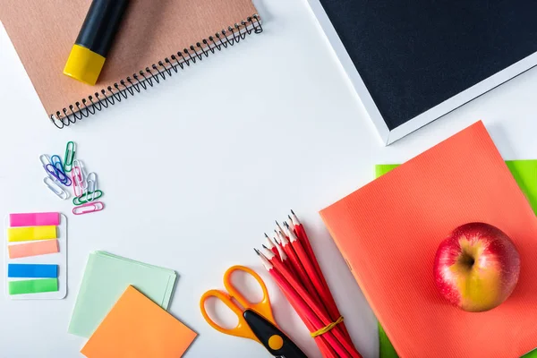 Top view of apple, empty chalkboard and variety school supplies on white background — Stock Photo