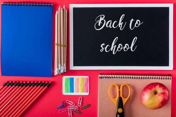 Top view of blackboard with lettering back to school, apple and arranged variety stationery on red background — Stock Photo