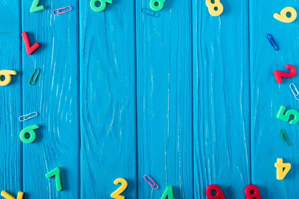 Vue de dessus de différents nombres colorés et trombones sur fond en bois bleu — Photo de stock